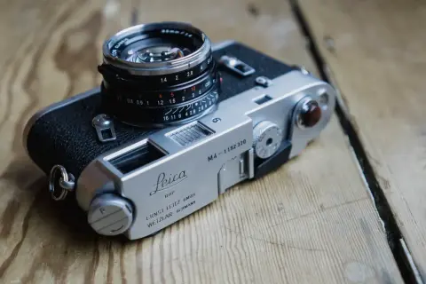 A classic Leica M4-P camera with a Summicron lens sits on a wooden surface.