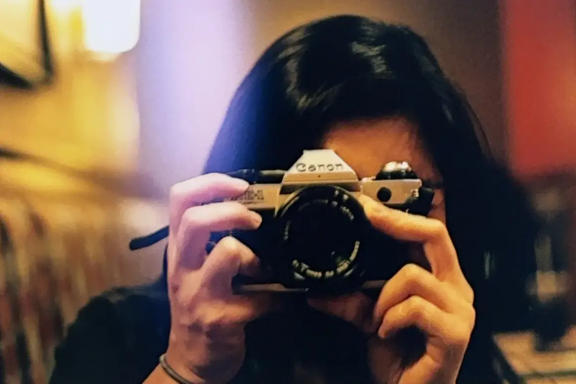 A person holds a Canon AE-1, a classic camera, ready to capture a moment. This camera is the best film for Canon AE-1 enthusiasts.