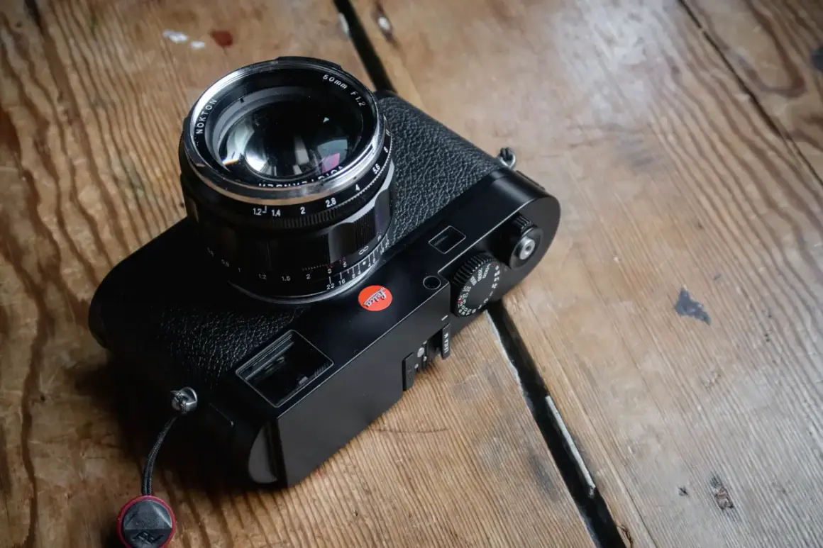 A black Leica M262 camera with a Nokton 50mm f/1.2 lens sits on a wooden surface.