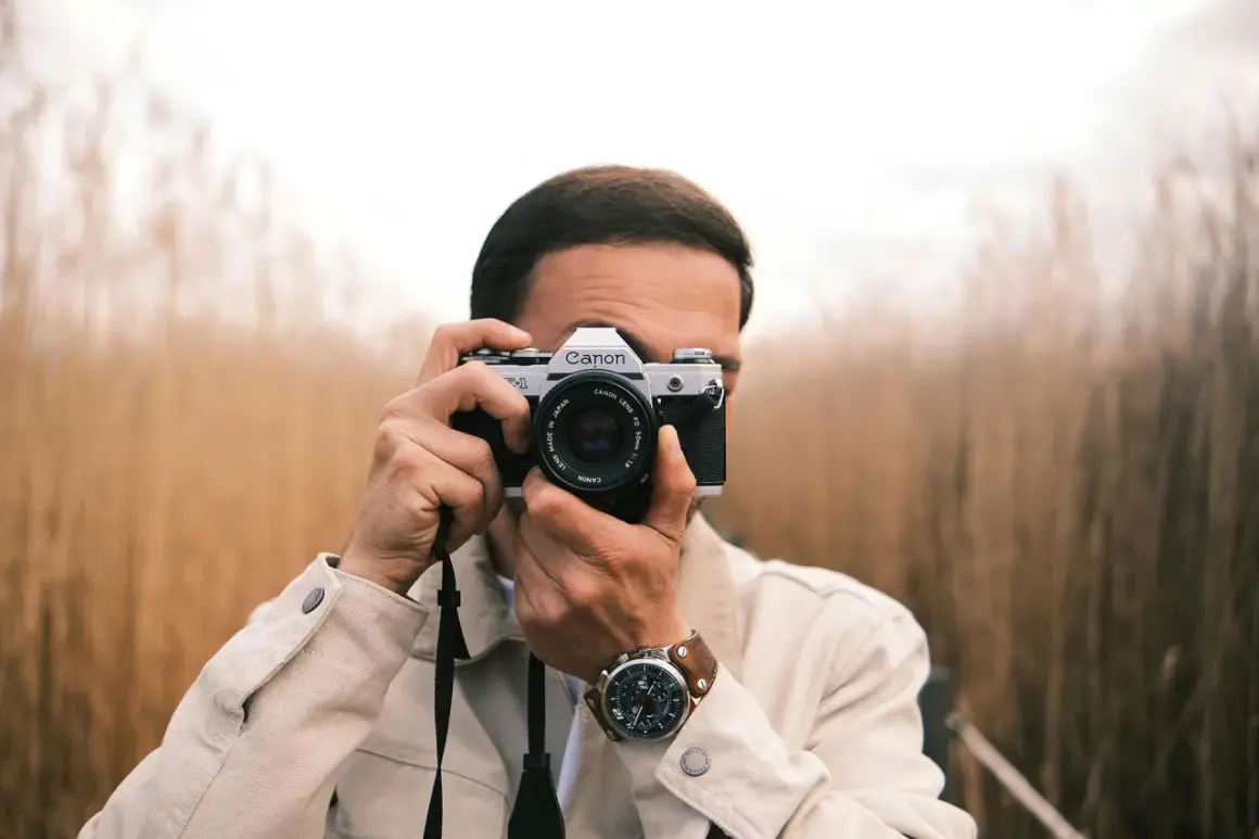 Man with a Canon AE-1, a classic choice for the best film camera for street photography, captures the moment amidst tall grasses.