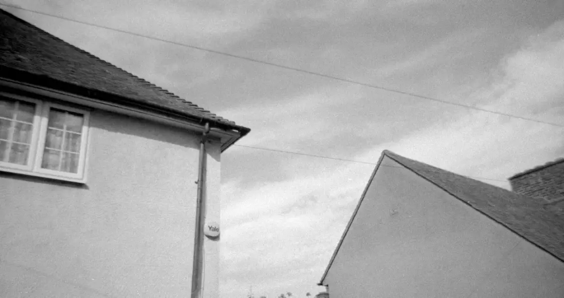 A black and white shot of two houses, captured on Kentmere 400 film. The image shows the roofs and walls of two buildings against a cloudy sky.