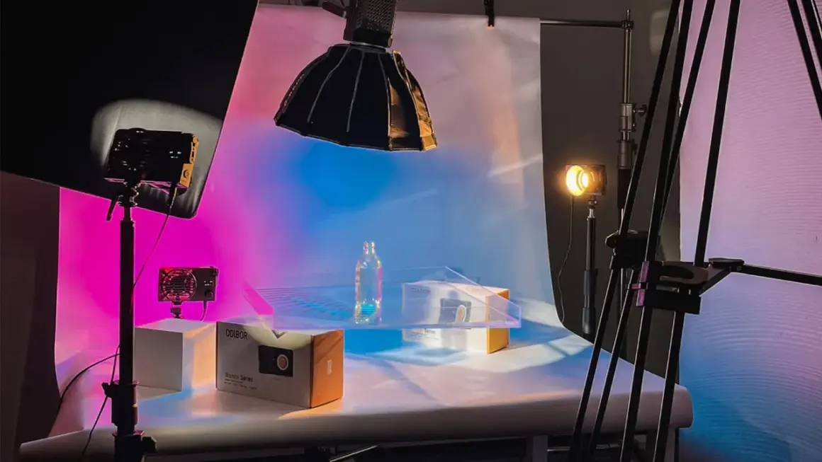Product photography setup with a bottle and boxes on a table, illuminated by colorful background light and studio lights.