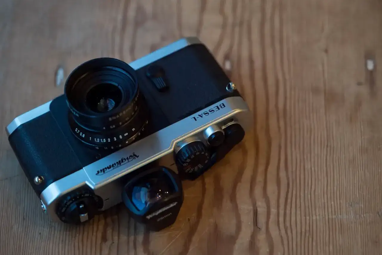 A Voigtlander Bessa L camera with a lens attached and a separate 28mm lens on a wooden surface.