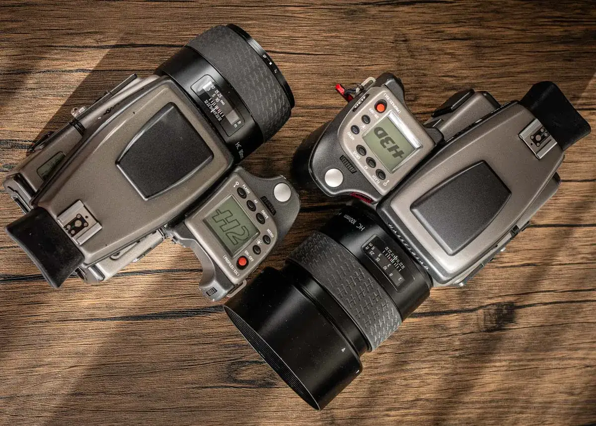 Two Hasselblad H2 camera bodies with lenses and accessories are laid out on a wooden surface.