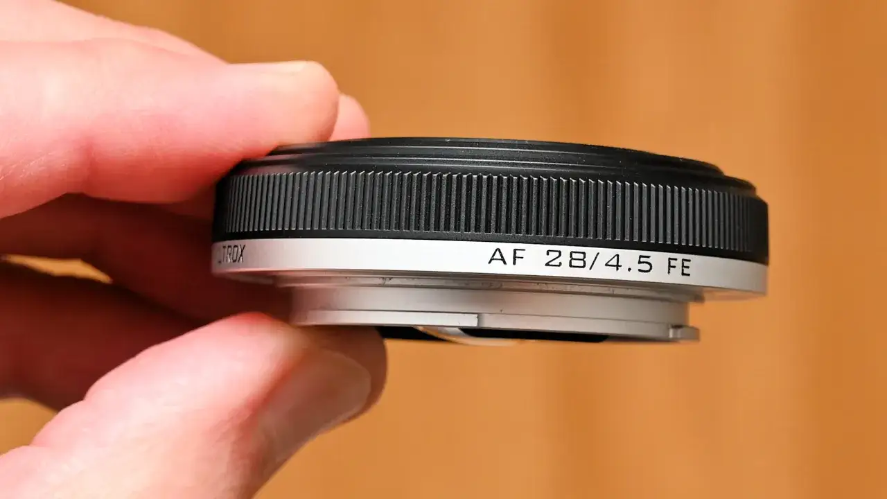 A hand holds a compact AF 28/4.5 FE lens, one of the many micro 4/3 pancake lenses available for photographers.