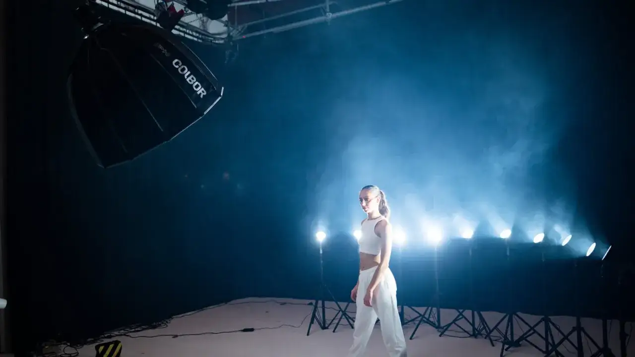 Fashion lighting photography in action: a model poses amidst dramatic smoke and studio lights, with a large softbox overhead.
