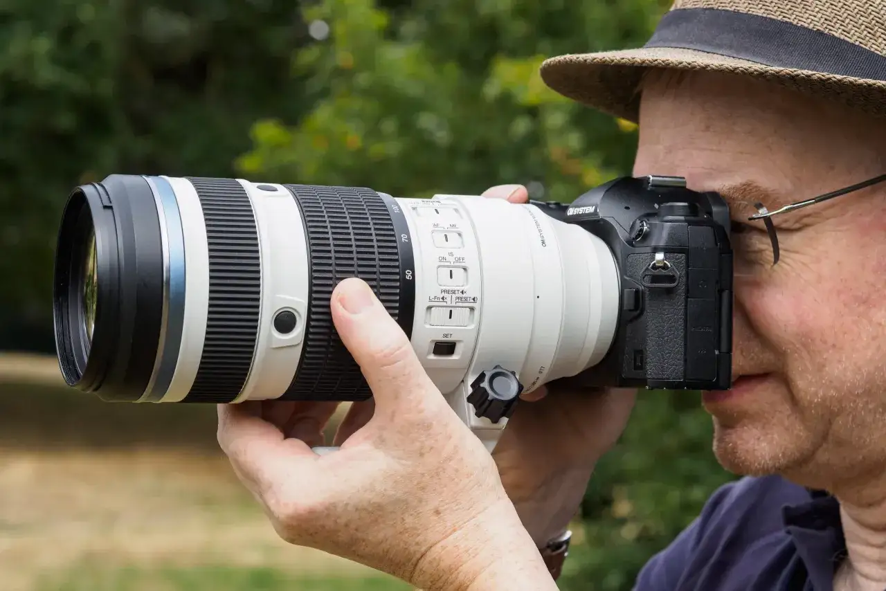 A photographer in a hat uses a camera with a large white lens, featuring zoom markings from 50 to 100mm. This lens is among the best 4 3 lenses for capturing distant subjects.