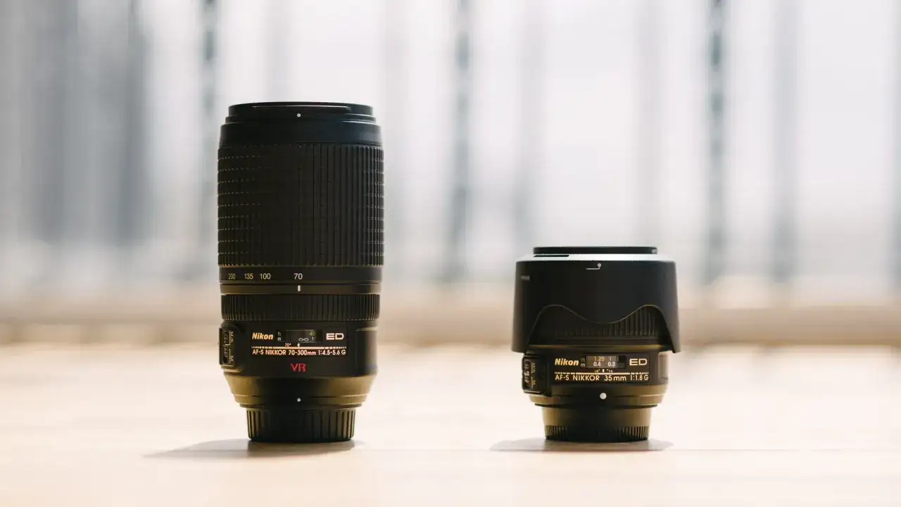 A Nikon telephoto lens and a Nikon wide-angle lens sit side-by-side, showcasing the difference in their size and focal length capabilities.